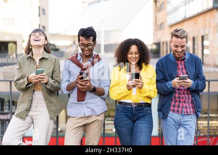 Multirassische Freunde, die im Universitätsviertel der Stadt mit dem Smartphone lachen - Junge Menschen, die von Mobiltelefonen süchtig sind - Technologie-Conce Stockfoto