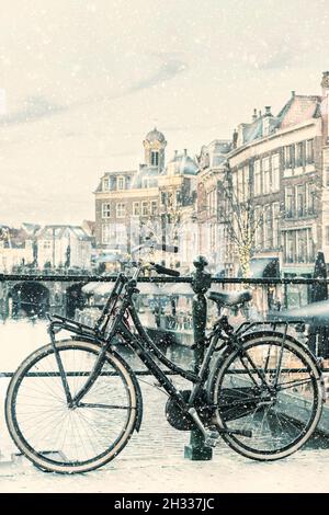 Winteransicht mit Schneefall des niederländischen Nieuwe Rijn Kanals mit Brücke und Fahrrad im Stadtzentrum von Leiden, Niederlande Stockfoto