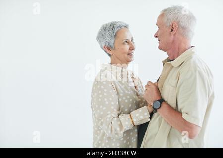 Glückliches älteres Paar, das sich mit Liebe anschaut und vor dem weißen Hintergrund tanzt Stockfoto