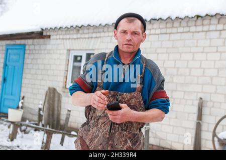 Russischer junger Mann, der draußen auf dem Hintergrund der Winterlandschaft steht. Bauarbeiter mit Telefon. Kaukasischer Arbeiter 40 Jahre alt, Porträt. Stockfoto