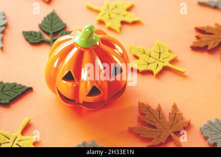 Deko orange kleines Lächeln Halloween Kürbis mit Herbst Ahorn Eiche Filzblätter von gelb rot braun und grün Farben in der Nähe auf orangefarbenem Hintergrund und Stockfoto