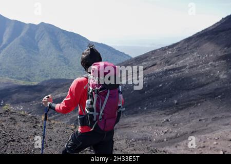 Foto eines Kletterers in rotem Hemd und Tasche, der auf den Berg blickt Stockfoto