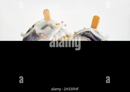 Nahaufnahme von Rollmops aus Heringsfilet und eingelegten Gurken mit Zwiebeln auf einem weißen Tisch Stockfoto