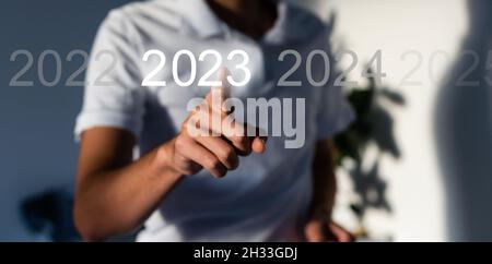 Fingerdruck der blauen Start 2023-Taste auf der virtuellen Benutzeroberfläche auf grauem Hintergrund mit Platz für Text. Konzept des neuen Jahres. Businessman Pressing Stockfoto