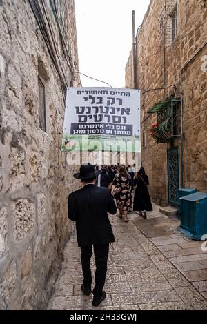 Ein religiöser Jude hält ein Schild mit der Aufschrift „Ein glückseliges Leben ist nur ohne Internet und Filme“, während er durch eine Gasse im jüdischen Viertel in der Altstadt von Jerusalem, Israel, geht. Haredi-Gemeinden meiden routinemäßig moderne Technologien wie Internet und Smartphones. Ihre Argumentation ist, dass die immense Menge an Informationen korrumpieren kann, und mit der Fähigkeit, das Internet ohne Beobachtung durch die Gemeinschaft zu nutzen, kann zu Individuation führen. Stockfoto