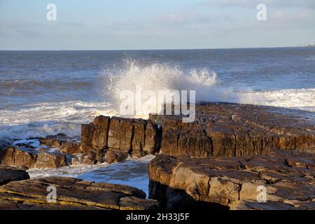 Ein sonniger Tag, an dem die Flut kommt und ziemlich kleine Wellen in die Felsen spritzen. Stockfoto
