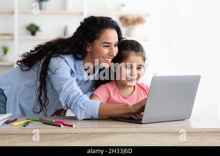 Liebevolle Mutter Hilft Ihr Nette Tochter Mit Online-Hausarbeit Während Fernstudium, Arabische Mutter Und Weibliches Kind Mit Laptop-Computer Für Remote Stud Stockfoto