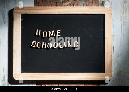 Frontale Nahaufnahme einer kleinen schwarzen Kreidetafel aus Holzbuchstaben mit den Worten Home Schooling auf einer hölzernen Oberfläche im rauen Seitenlicht. Stockfoto