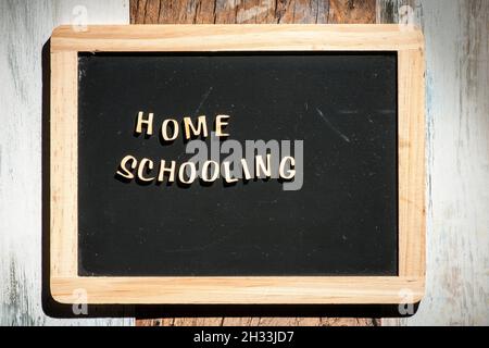 Frontale Nahaufnahme einer kleinen schwarzen Kreidetafel aus Holzbuchstaben mit den Worten Home Schooling auf einer hölzernen Oberfläche im rauen Seitenlicht. Stockfoto