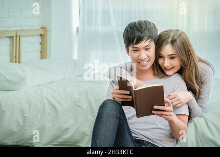 Glücklicher asiatischer Liebhaber oder Paar beim Lesen des Notebooks auf dem Bett im Schlafzimmer zu Hause, Paar und Lifestyle-Konzept, Stockfoto