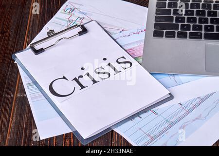 Zwischenablage mit Krisenwort und Laptop auf dem Schreibtisch. Stockfoto