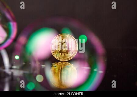 Goldene Bitcoin-Münze, die auf einer reflektierenden Schreibtischoberfläche steht. Stockfoto