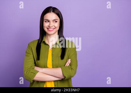 Foto von charmanten niedlichen jungen Dame gekleidet grünen Kleidung Arme gekreuzt suchen leeren Raum lächelnd isoliert lila Farbe Hintergrund Stockfoto