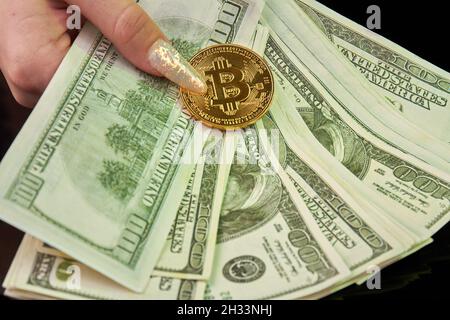 Nahaufnahme der weiblichen Hand hält Dollarnoten und Bitcoin. Stockfoto