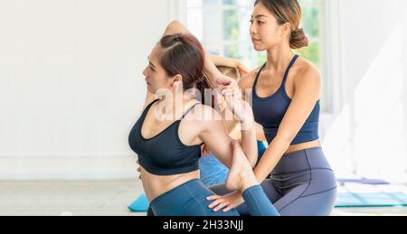 Gruppe von Vielfalt Yoga Sport Menschen üben mit ihrem Coaching in Yoga-Klasse, asiatische Yoga-Ausbilderin Frau unterstützen jungen asiatischen Sportmann für Yoga tr Stockfoto