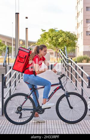 Eine Radfahrerin überprüft die Adresse ihrer nächsten Lieferung mit ihrem Mobiltelefon Stockfoto