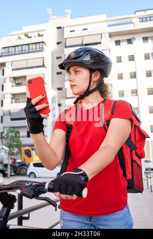 Eine Radfahrerin überprüft die Adresse ihrer nächsten Lieferung mit ihrem Mobiltelefon Stockfoto