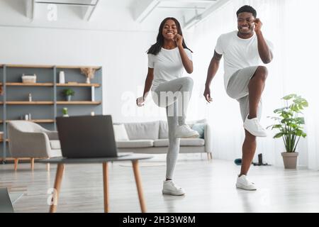 Online-Training Für Die Familie. Afroamerikanischer Ehemann Und Ehefrau Trainieren Gemeinsam Im Wohnzimmer Und Üben Dabei „Knie Drehen“ Bis „Ellenbogen“. Happy Black steht Ein Stockfoto
