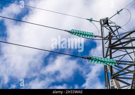 Nahaufnahme eines transparenten türkisfarbenen Hochspannungsisolators oder Isolators in Sonnenlicht auf einem elektrischen Turm auf blauem Himmel Hintergrund. Stockfoto