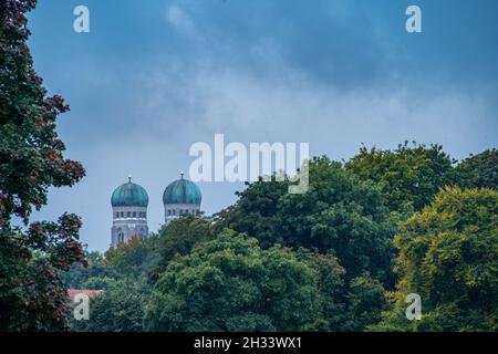 Blick auf die Gipfel der beiden beliebten Türme der Frauenkirche in München, bayern, über grüne und herbstliche Baumkronen. Stockfoto