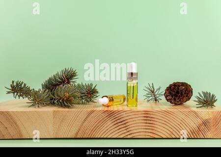 Aromatherapie- und Spa-Komposition mit ätherischem Fichtenöl in kleinen Glasflaschen, grünen Zweigen und Kegel auf Holzboxholz stehen auf hellgrünem Rücken Stockfoto