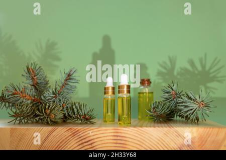 Kreative weihnachtliche Aromatherapie- und Spa-Komposition mit trendigen Schatten. Ätherisches Nadelfichtenöl in kleinen Glasflaschen und grünen Zweigen auf Woo Stockfoto