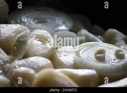 Bratvorgang von Kartoffeln mit frischen Zwiebeln in der gusseisernen Pfanne Stockfoto