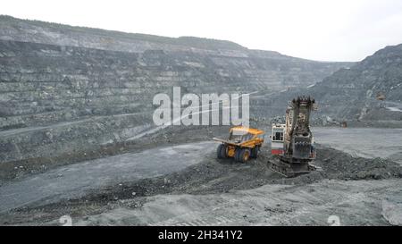 Bagger füllt Muldenkipper mit Erde im Tagebau. Schwere Maschinen arbeiten in der Bergbauindustrie im Tagebau Stockfoto
