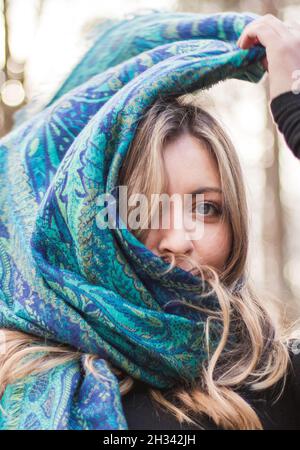 Blonde junge Erwachsene mit blauen Augen und schwarzem Top trägt blauen Schal im Wald Stockfoto