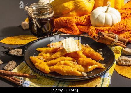 Faule Kürbisknödel, Gnocchi mit Butter und braunem Zucker. Warmes Herbstgericht, süße gesunde Lebensmittel. Schwarzer Stein Beton Hintergrund, trendy hartes Licht, Stockfoto