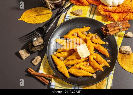 Faule Kürbisknödel, Gnocchi mit Butter und braunem Zucker. Warmes Herbstgericht, süße gesunde Lebensmittel. Schwarzer Stein Beton Hintergrund, trendy hartes Licht, Stockfoto