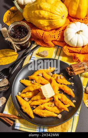 Faule Kürbisknödel, Gnocchi mit Butter und braunem Zucker. Warmes Herbstgericht, süße gesunde Lebensmittel. Schwarzer Stein Beton Hintergrund, trendy hartes Licht, Stockfoto