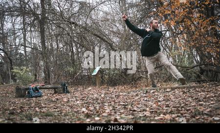 Sportlicher junger Mann, der im Winter im Wald Disc Golf spielt Stockfoto