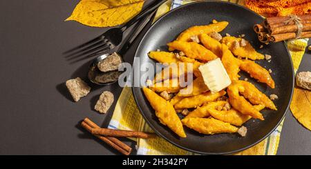 Faule Kürbisknödel, Gnocchi mit Butter und braunem Zucker. Warmes Herbstgericht, süße gesunde Lebensmittel. Schwarzer Stein Beton Hintergrund, trendy hartes Licht, Stockfoto