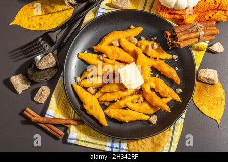 Faule Kürbisknödel, Gnocchi mit Butter und braunem Zucker. Warmes Herbstgericht, süße gesunde Lebensmittel. Schwarzer Stein Beton Hintergrund, trendy hartes Licht, Stockfoto