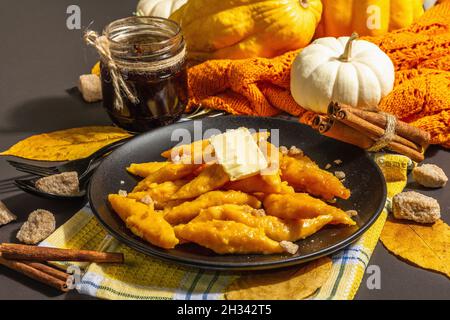 Faule Kürbisknödel, Gnocchi mit Butter und braunem Zucker. Warmes Herbstgericht, süße gesunde Lebensmittel. Schwarzer Stein Beton Hintergrund, trendy hartes Licht, Stockfoto