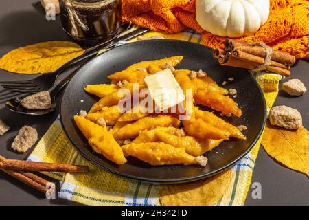 Faule Kürbisknödel, Gnocchi mit Butter und braunem Zucker. Warmes Herbstgericht, süße gesunde Lebensmittel. Schwarzer Stein Beton Hintergrund, trendy hartes Licht, Stockfoto