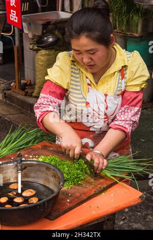 Eine Frau schneidet grüne Zwiebeln in einer Outdoor-Küche auf dem Straßenmarkt in der Altstadt von Shanghai, China. Stockfoto
