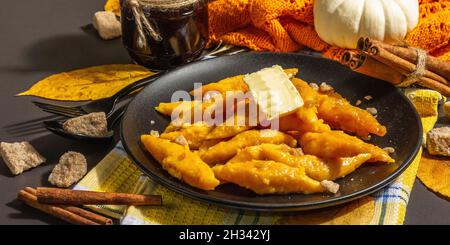 Faule Kürbisknödel, Gnocchi mit Butter und braunem Zucker. Warmes Herbstgericht, süße gesunde Lebensmittel. Schwarzer Stein Beton Hintergrund, trendy hartes Licht, Stockfoto