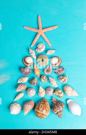 Viele kleine verschiedene Muscheln und ein Seesterne sind in Form eines Weihnachtsbaums auf lackiertem türkisfarbenem Holzhintergrund angelegt. Alternativer Weihnachtsbaum Stockfoto