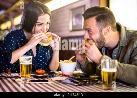 Glückliches Paar, das Spaß beim Burger-Essen im Restaurant Pub Fast Food hat - Junge Leute genießen Momente im Restaurant - Beziehungskonzept Stockfoto