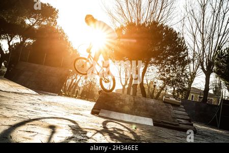 Urban Athlet Biker Durchführung akrobatischen Sprung im öffentlichen Park - Guy Reiten bmx Fahrrad bei Extremsportwettbewerb am sonnigen Nachmittag Stockfoto