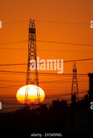 Strommasten und Stromleitungen bei Sonnenaufgang mit großer Sonne am Horizont. Portugal, Europa Stockfoto