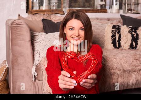 Frau hält das Herz in ihren Händen und lächelt. Valentinstag zu Hause Konzept. Stockfoto