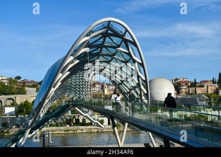 Tiflis, Georgien - 24. Oktober 2021: Die Brücke des Friedens, bogenförmige Fußgängerbrücke über den Fluss Kura in der georgischen Hauptstadt. Stahl und Glas Stockfoto