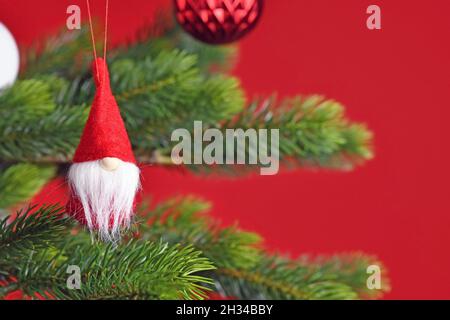 Geschmückter Weihnachtsbaum mit niedlichem Weihnachtsgnome-Baumschmuck auf rotem Hintergrund Stockfoto