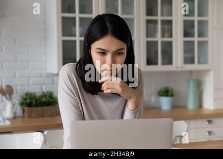 Ernst fokussierter asiatischer Student mit Laptop in der Küche Stockfoto