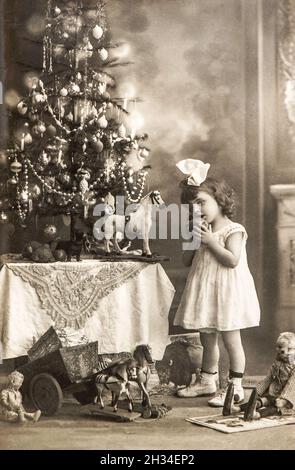 Littele Mädchen mit Weihnachtsbaum und Vintage-Spielzeug. Alte Fotopostkarte Stockfoto
