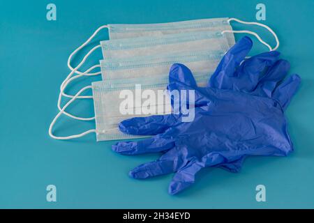 Vier neue medizinische Masken und ein Paar blaue Nitrilhandschuhe stehen auf dem Tisch. Persönliche Schutzausrüstung bei einer Pandemie Stockfoto