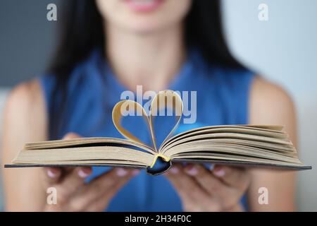 Bei weiblichen Händen werden die Buchblätter in Form einer Nahaufnahme des Herzens gefaltet Stockfoto